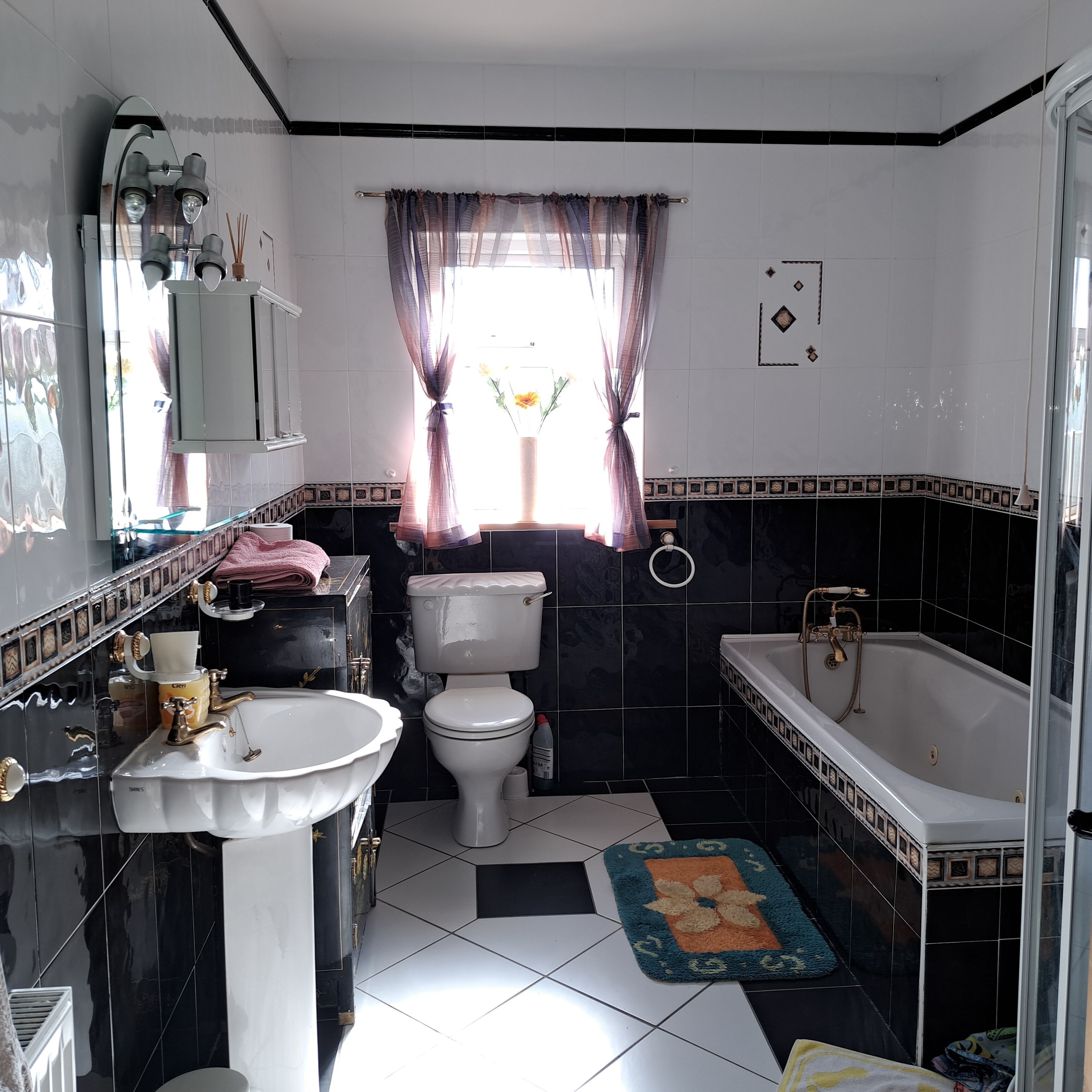 A bathroom with a white sink, toilet, and bathtub. There is a window with curtains, a mirror, and a towel rack.