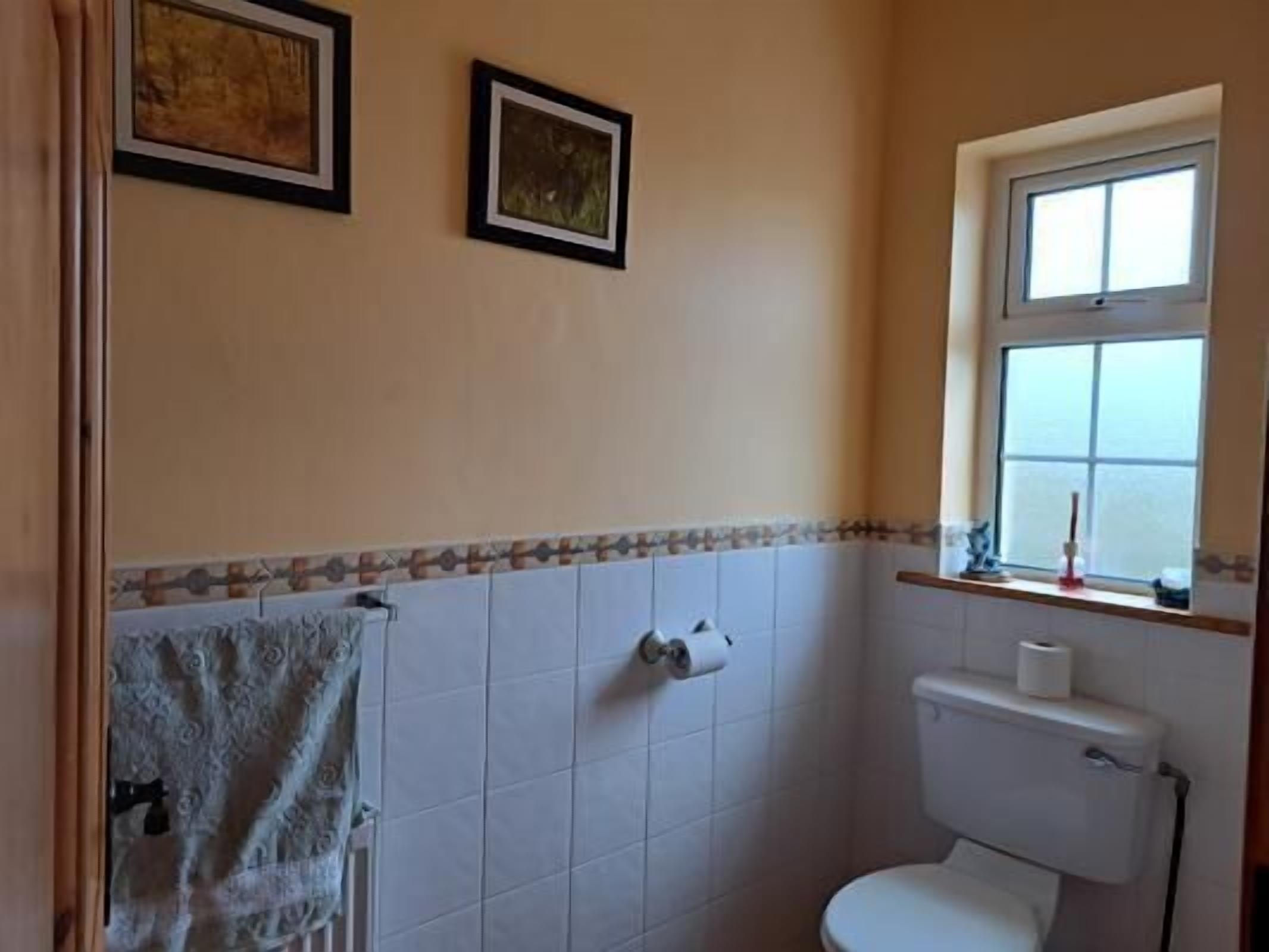 A small bathroom with a toilet, a window, and two framed pictures on the wall.