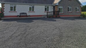 A two-story house with a gravel driveway, a stone exterior, and a small porch with a bench. - Spacious 6-bed House 10 Minutes From Knock Airport (Kilmovee)