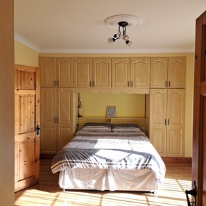 A bedroom with a bed, wooden wardrobe, and a ceiling light fixture.