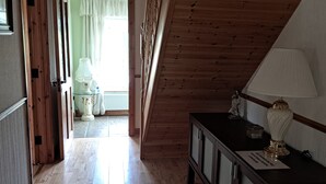 A hallway with wooden flooring and a sloped ceiling. There is a cabinet with a lamp on it and a sign on the floor. - Spacious 6-bed House 10 Minutes From Knock Airport (Kilmovee)