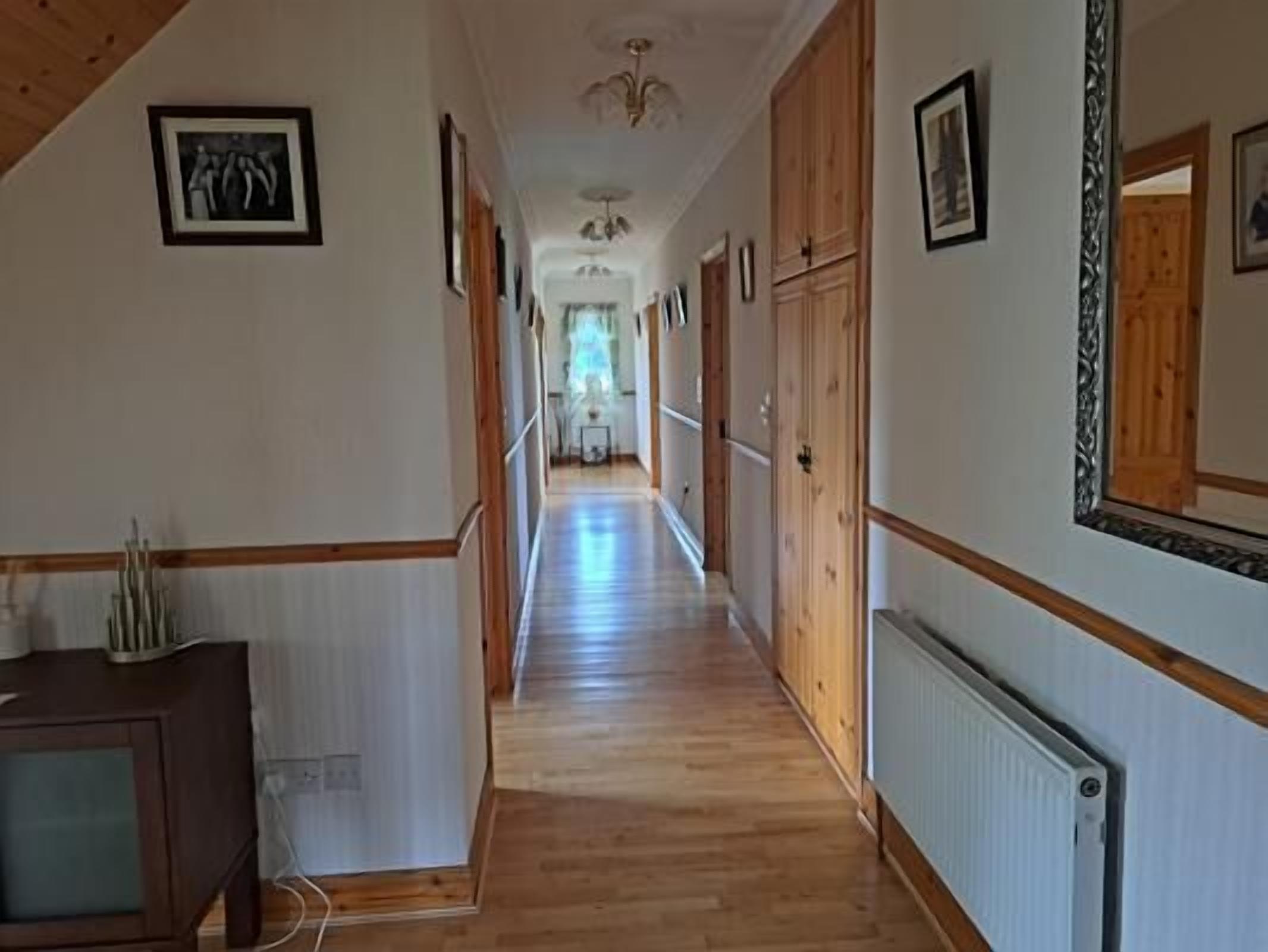 A long, narrow hallway with wooden floors and walls, flanked by wooden cabinets and framed pictures.