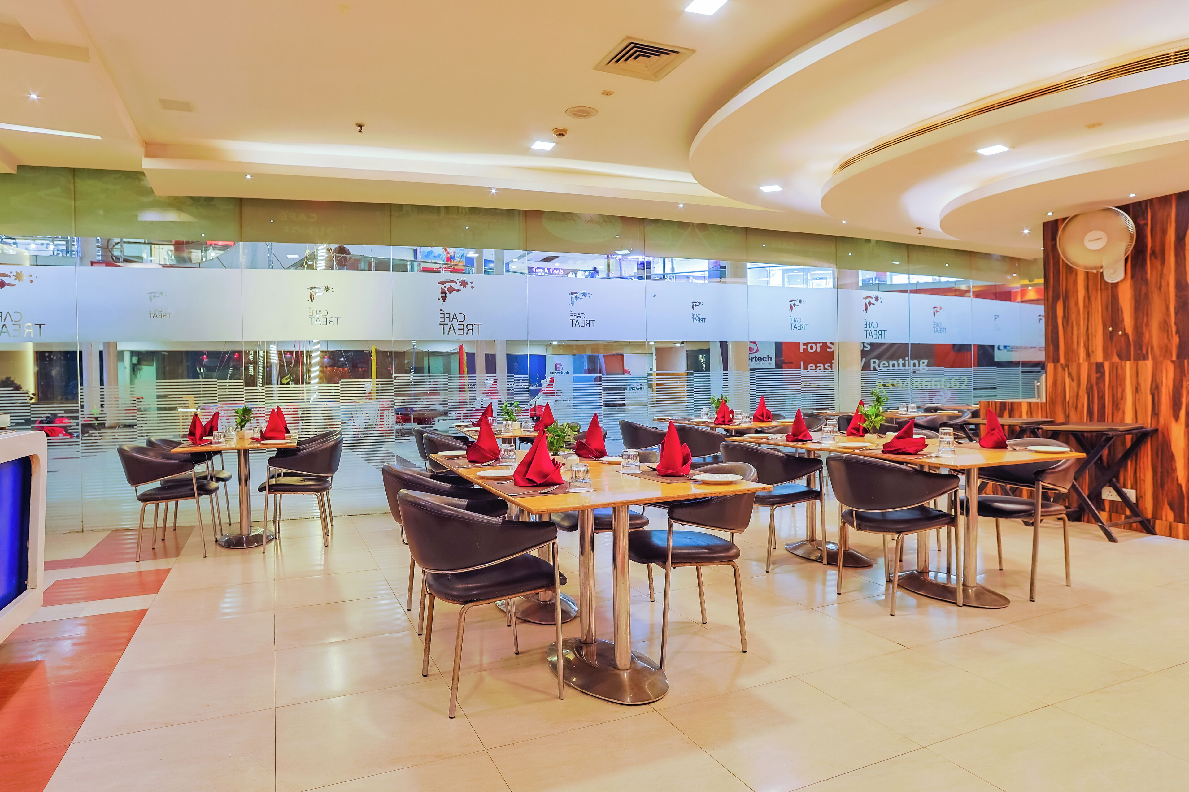 Un restaurante moderno con varias mesas y sillas, un balcón en el segundo piso y una pared decorativa de madera.