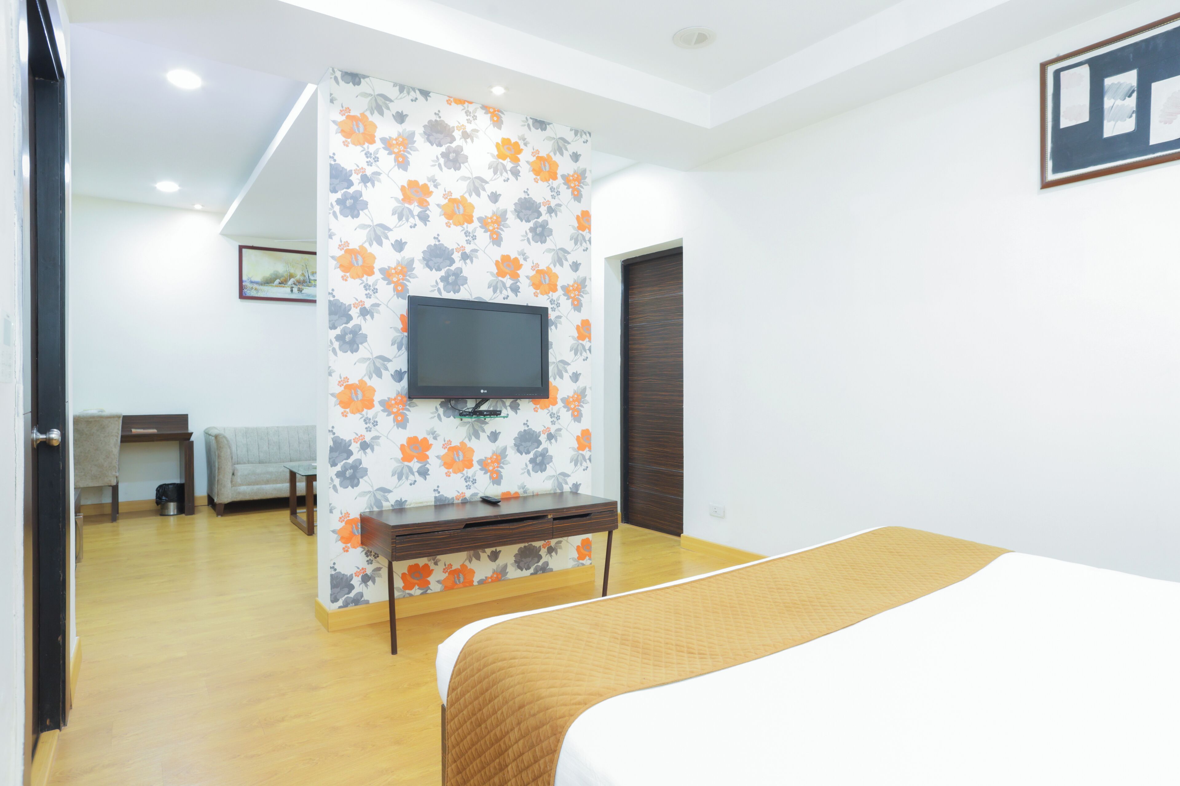 Un dormitorio con cama, televisor montado en una pared con estampado floral, escritorio de madera y sofá.