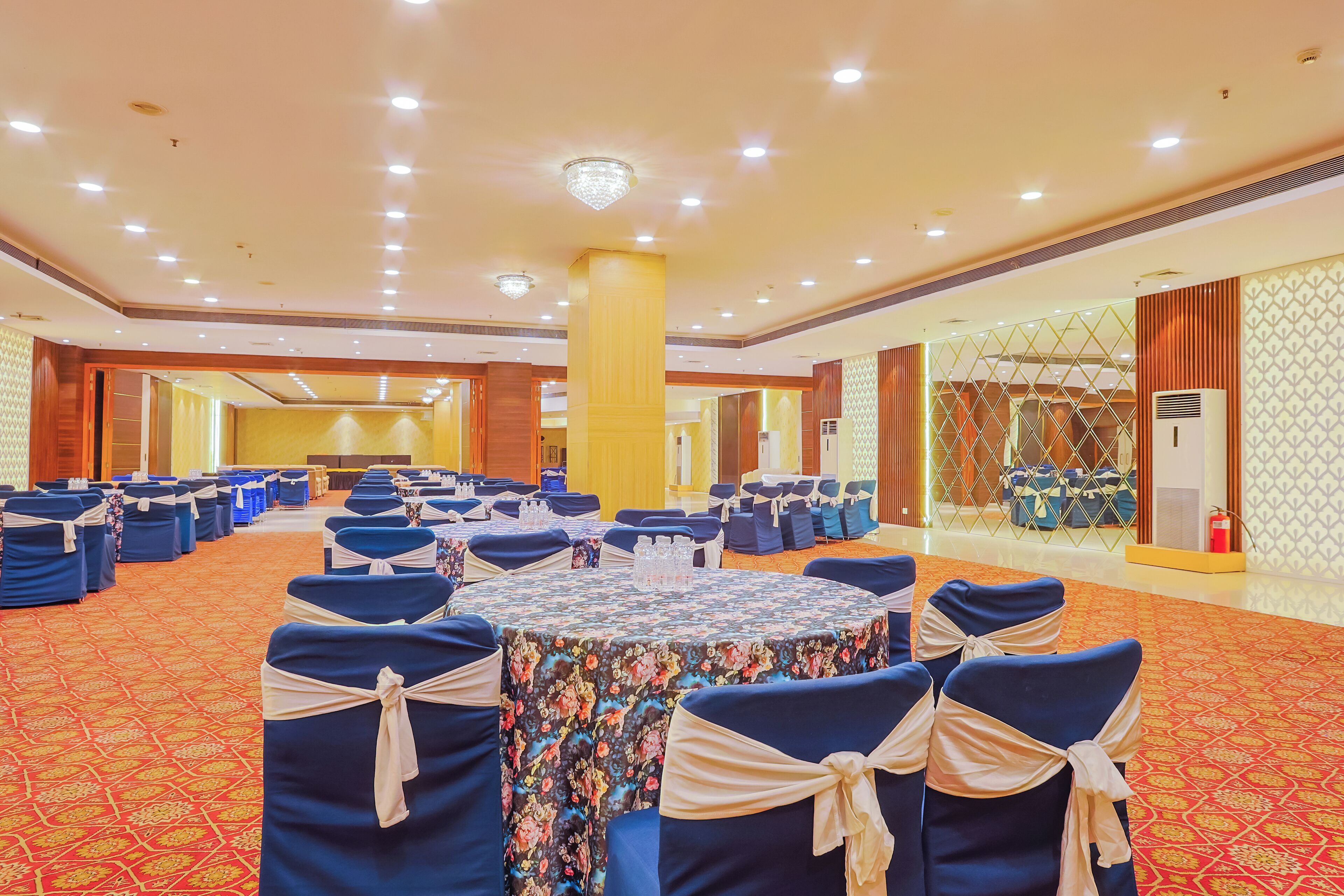 A large conference room with round tables, blue chairs with white sashes, and a patterned carpet.