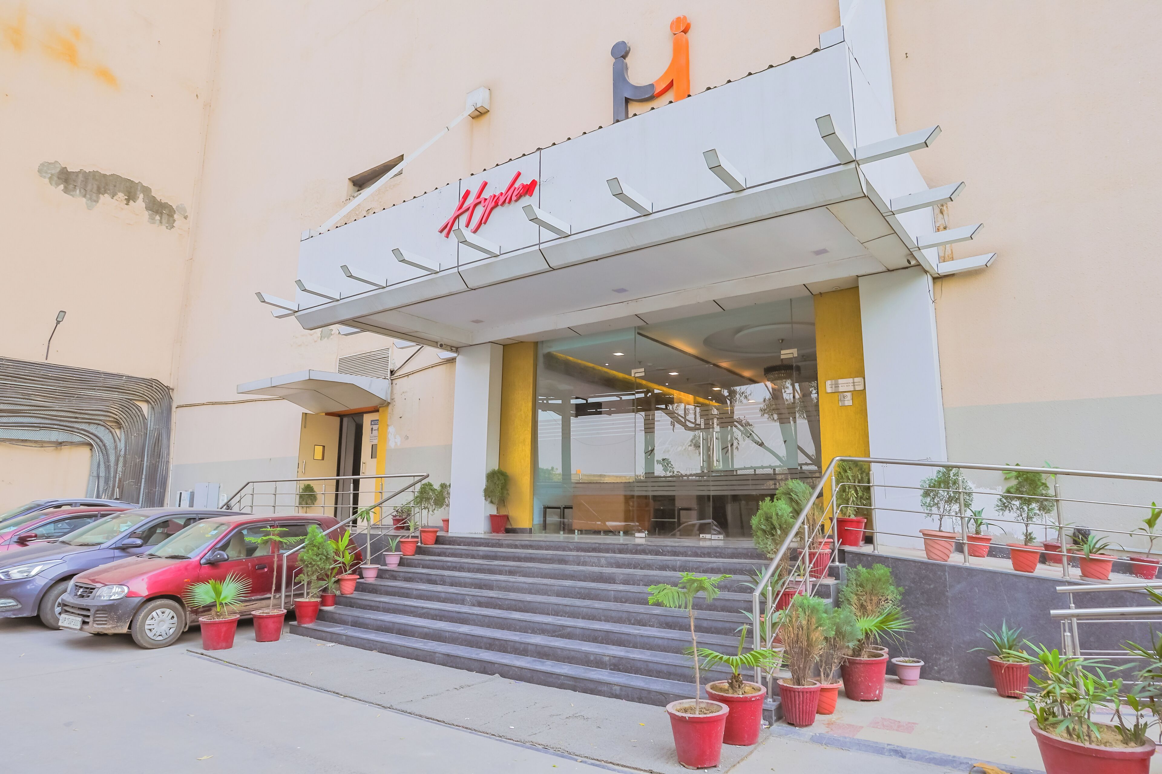 A hotel entrance with a staircase leading up to the door, potted plants, and a parked car.