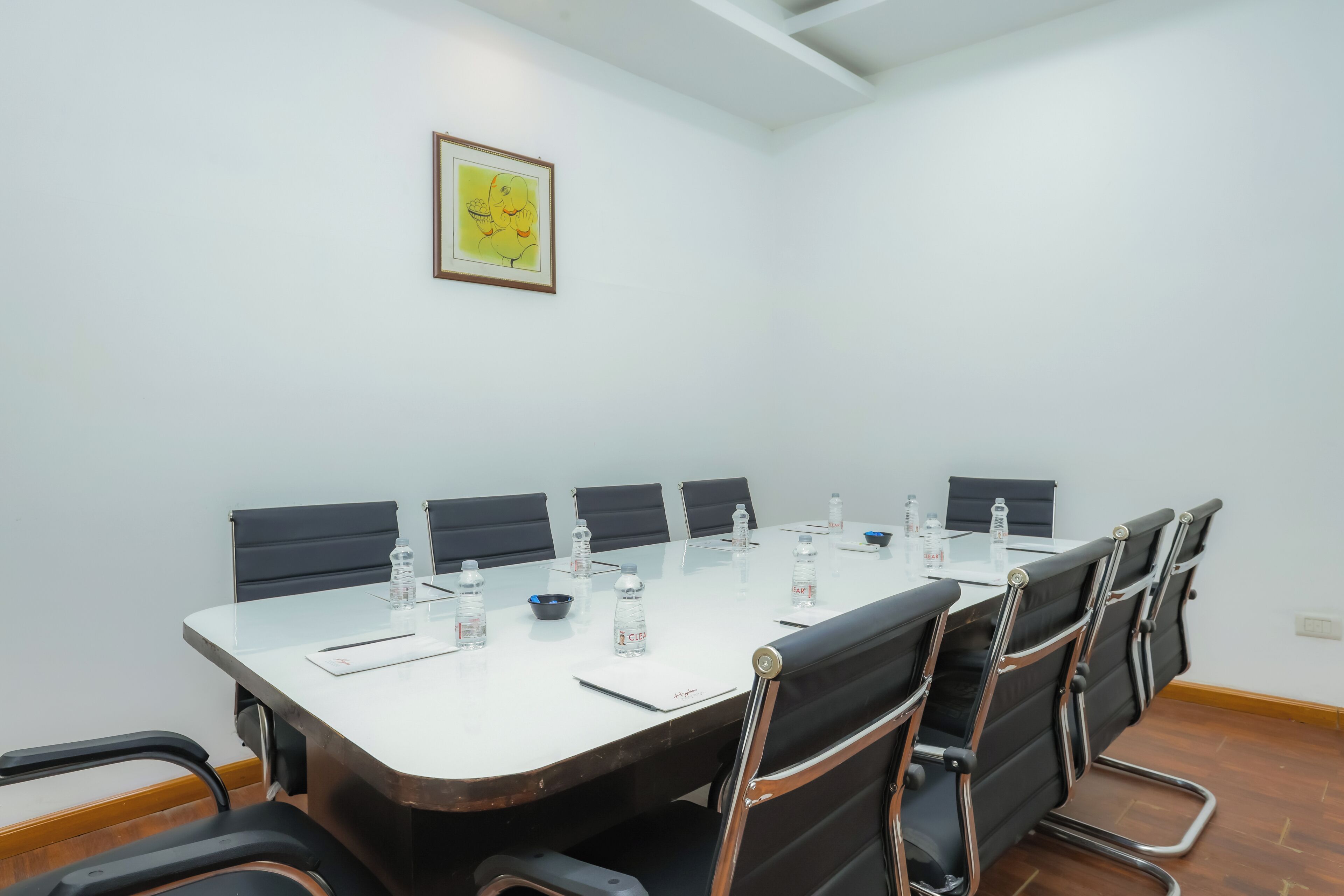 A conference room with a long table, black chairs, water bottles, and a framed picture on the wall.
