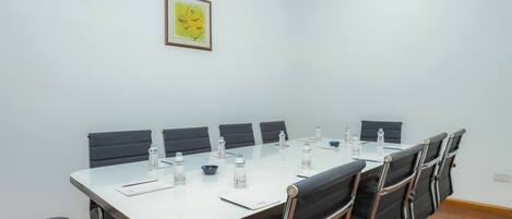 A conference room with a long table, black chairs, water bottles, and a framed picture on the wall.