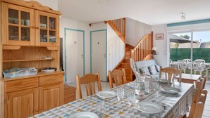 Zona pranzo con tavolo di legno apparecchiato per quattro persone, una scala e vista sull'esterno.