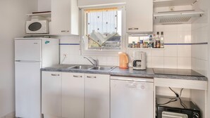 Una cucina compatta con mobili bianchi, forno a microonde integrato, macchina del caffè e tostapane.