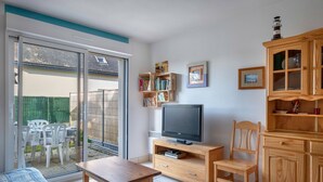 Un soggiorno con televisore, mobili in legno, una porta scorrevole in vetro che dà su un patio e una libreria.