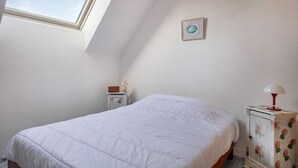 Una camera da letto con un lucernario, un letto, un comodino, un armadio e un quadro appeso alla parete.