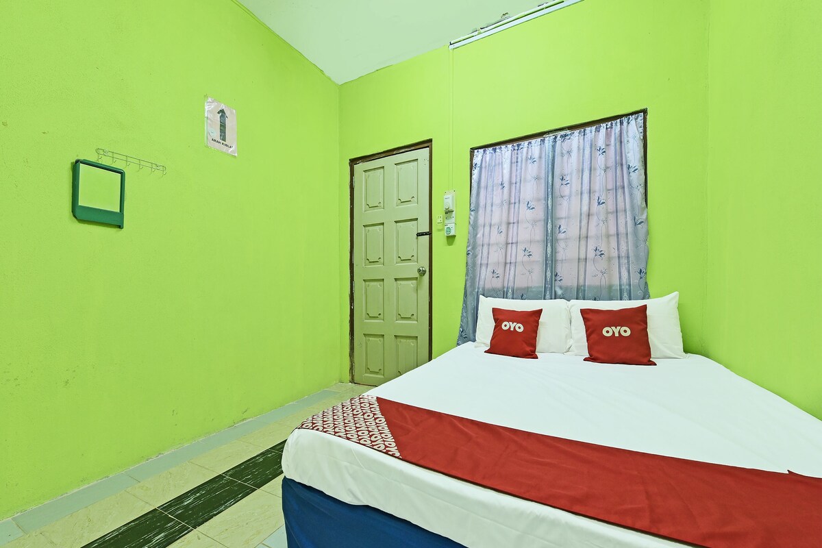 A room with a bed, a door, a window with curtains, and a wall-mounted light fixture.