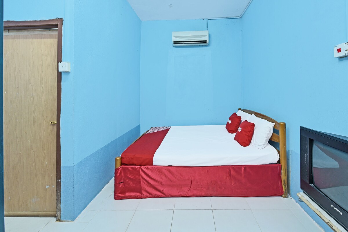 A small, single-bed room with a wooden door, a built-in TV, and a ceiling fan.