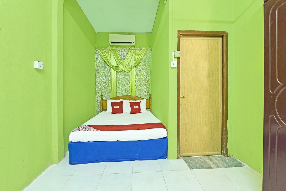 A small, brightly colored room with a bed, a door, and a wall-mounted air conditioner.