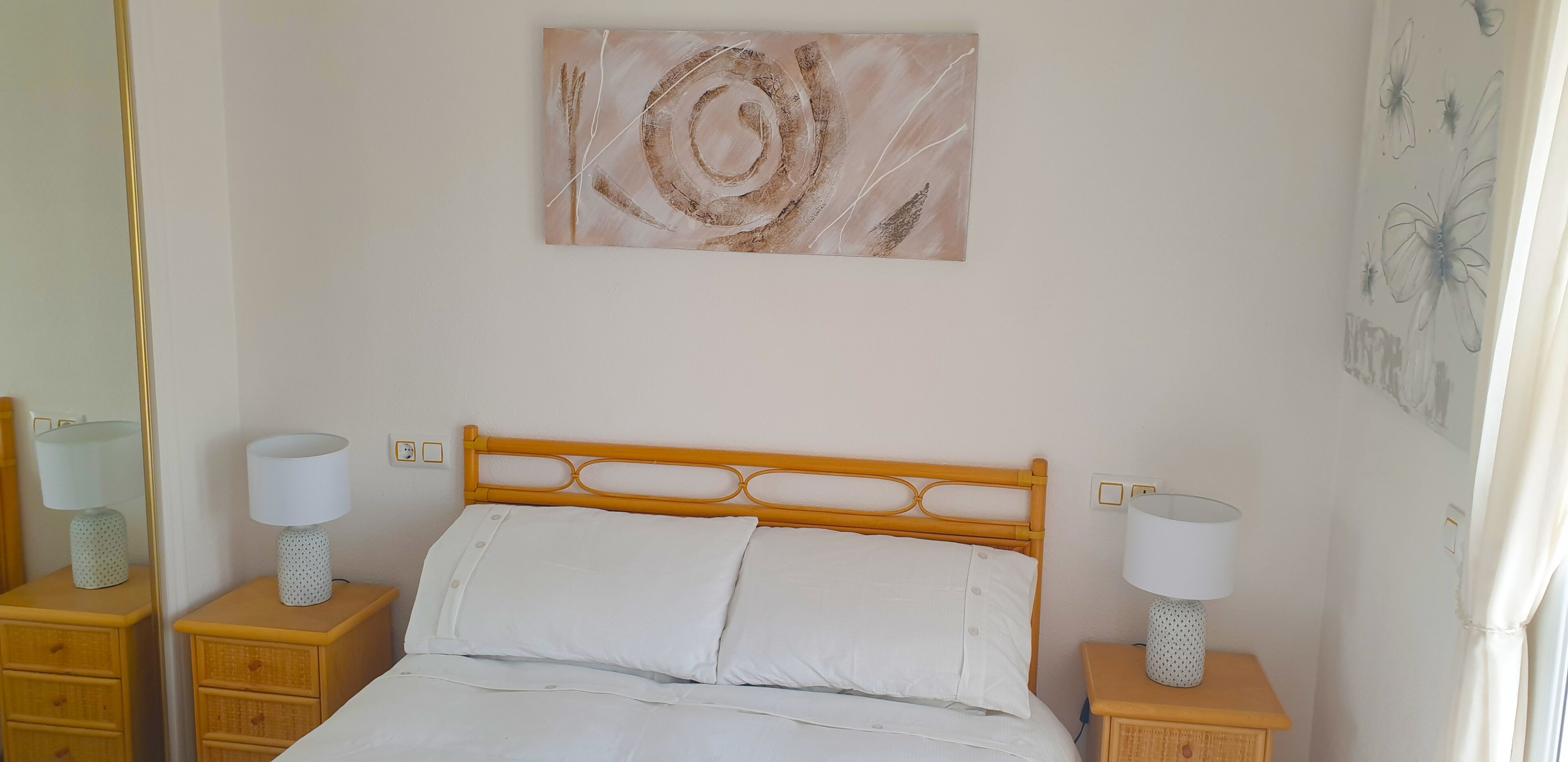 Una cama bien hecha con sábanas blancas, un cabecero de madera y dos lámparas de noche sobre mesitas de noche de madera.