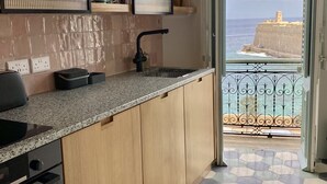 Een keuken met houten kastjes, een granieten aanrechtblad en uitzicht op zee door een open deur.