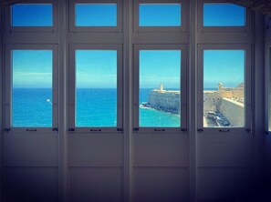 Blick durch mehrere Fenster auf eine Küstenlandschaft mit Leuchtturm und Befestigungsanlagen.