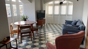 Een woonkamer met een ronde tafel, stoelen, een bank, een televisie en een potplant.