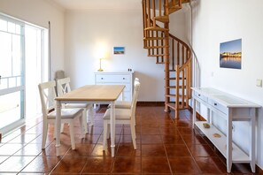 Un coin repas avec une table en bois, des chaises blanches, un buffet blanc et un escalier en colimaçon en bois.