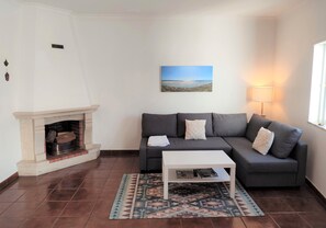 Un salon avec une cheminée, un canapé gris, une table basse blanche et un tapis à motifs.