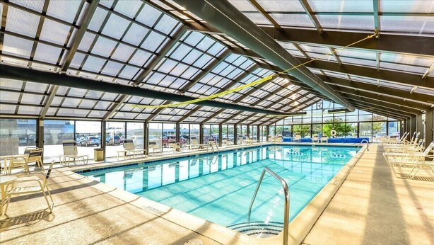En inomhuspool med ett tak av genomskinligt glas, ett soligt poolområde och solstolar.