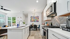 A modern kitchen with white cabinetry, a central island, a dining area with a table and chairs, and a colorful abstract painting on the wall. - Wow! 5-Star Luxury ~ Safe & 3M to DT ~ (Austin)