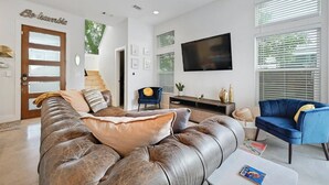 A modern living room with a leather sofa, a blue armchair, a flat-screen TV, and a staircase leading to another level. - Wow! 5-Star Luxury ~ Safe & 3M to DT ~ (Austin)