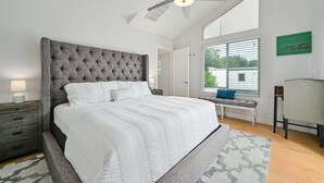 A bedroom with a large bed, a ceiling fan, a window with blinds, a bench, and a green sign on the wall. - Wow! 5-Star Luxury ~ Safe & 3M to DT ~ (Austin)