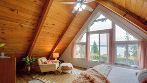 Une chambre mansardée chaleureuse avec un plafond en pente, une grande fenêtre avec des rideaux, un lit, une chaise et un bureau.