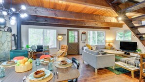 Un vaste salon doté d’un plafond en bois, un coin repas avec une table mise pour le repas, et un espace salon confortable.