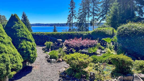 Un jardin avec un chemin de gravier, différents arbustes et arbres.