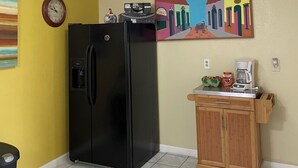 Una cocina con un refrigerador negro, un armario de madera, una cafetera y un reloj en la pared.