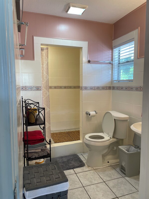 Un baño con ducha, inodoro, lavabo y un pequeño ventanal.