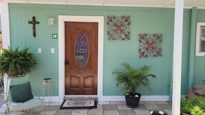 Fachada de una casa color turquesa con puerta de madera, planta en maceta y decoración mural.