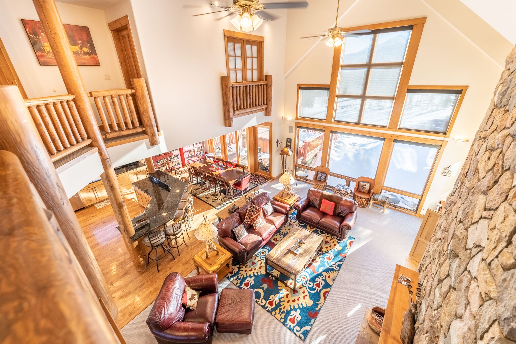 A spacious living area with a high ceiling, wooden staircase, and large windows offering a view of the outdoors.