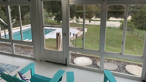 Une pièce dotée de grandes fenêtres donnant sur une piscine et un espace verdoyant avec un étang.