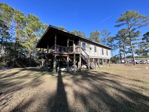 A two-story wooden cabin with a balcony, surrounded by trees and a grassy yard. - Eagle's Nest Sapelo Island, beach, nature & comfort (Sapelo Island)