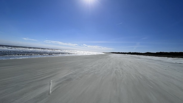 En bred, øde strand med en klar himmel og stærk solskin.