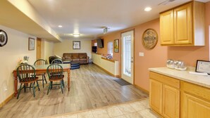 A spacious living area with a dining table, chairs, and a sofa. There is a kitchen area with wooden cabinets and a countertop.