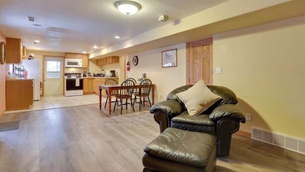 A spacious living area with a leather sofa, wooden dining table, and a kitchen in the background.