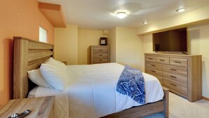 A bedroom with a bed, wooden headboard, bedside table, dresser, and a TV mounted on the wall.