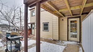 A covered patio area with a grill and propane tank, a door with glass panels, and a snow-covered ground.
