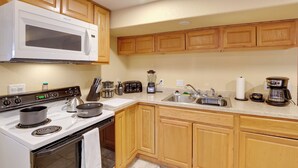 A kitchen with wooden cabinets, a white microwave, a stove, a sink, and various appliances like a toaster and a coffee maker.