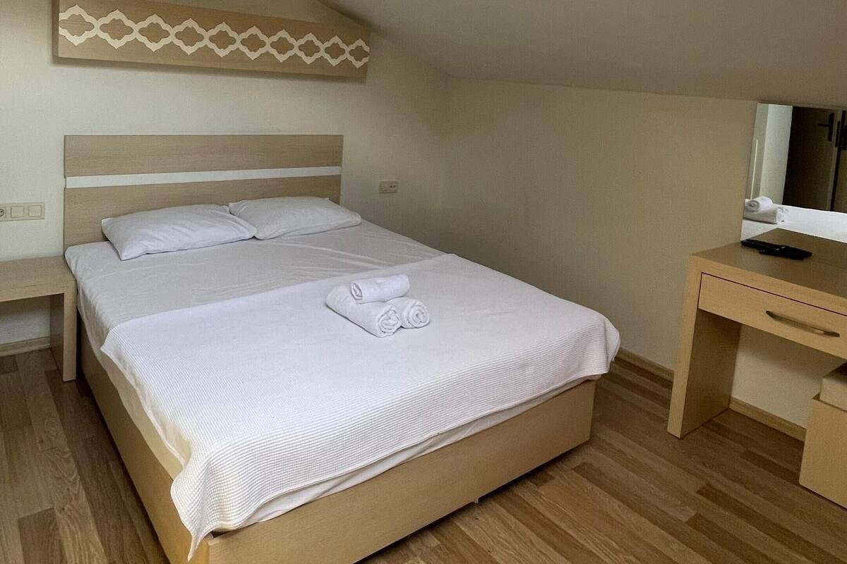 Quarto com claraboia, cama, escrivaninha e espelho.