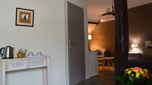 A hotel room with a bed, a desk with a lamp, a chair, and a small table with a kettle and cups. There is a framed picture on the wall and a vase with flowers on the floor. - La maison de Triboulet, bed and breakfast, Nutrisco, Nutrisco (Pocé-sur-Cisse)