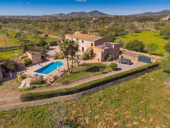 A villa with a swimming pool, a carport, and a stone wall.