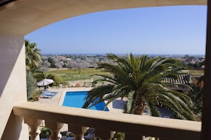 A balcony with a view of a swimming pool, palm trees, and a distant landscape.