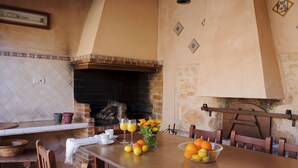 A dining area with a brick fireplace, wooden table, chairs, and a bowl of fruit. - Tanca - Typical Finca with Private Pool, Sleeps 8, A/C, Wi-Fi, Near Cala d'Or (Santanyí)