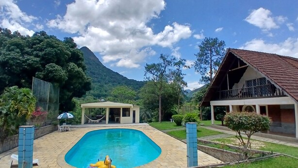 Una piscina con un'amaca e un cane gonfiabile giallo, immersa nel verde con una montagna sullo sfondo.